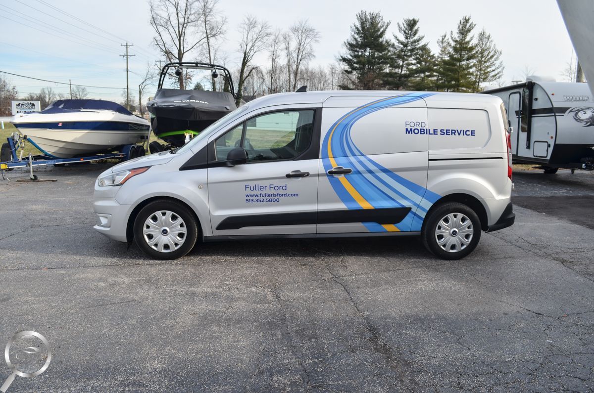 White service van with blue and yellow graphics parked outdoors near a boat and RVs.