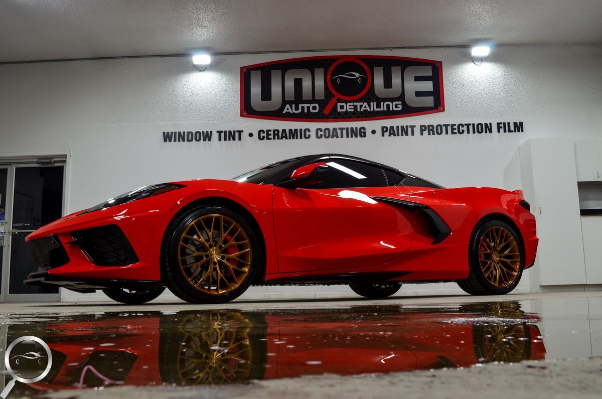 Red sports car in an auto detailing shop, with glossy reflection on the wet floor.