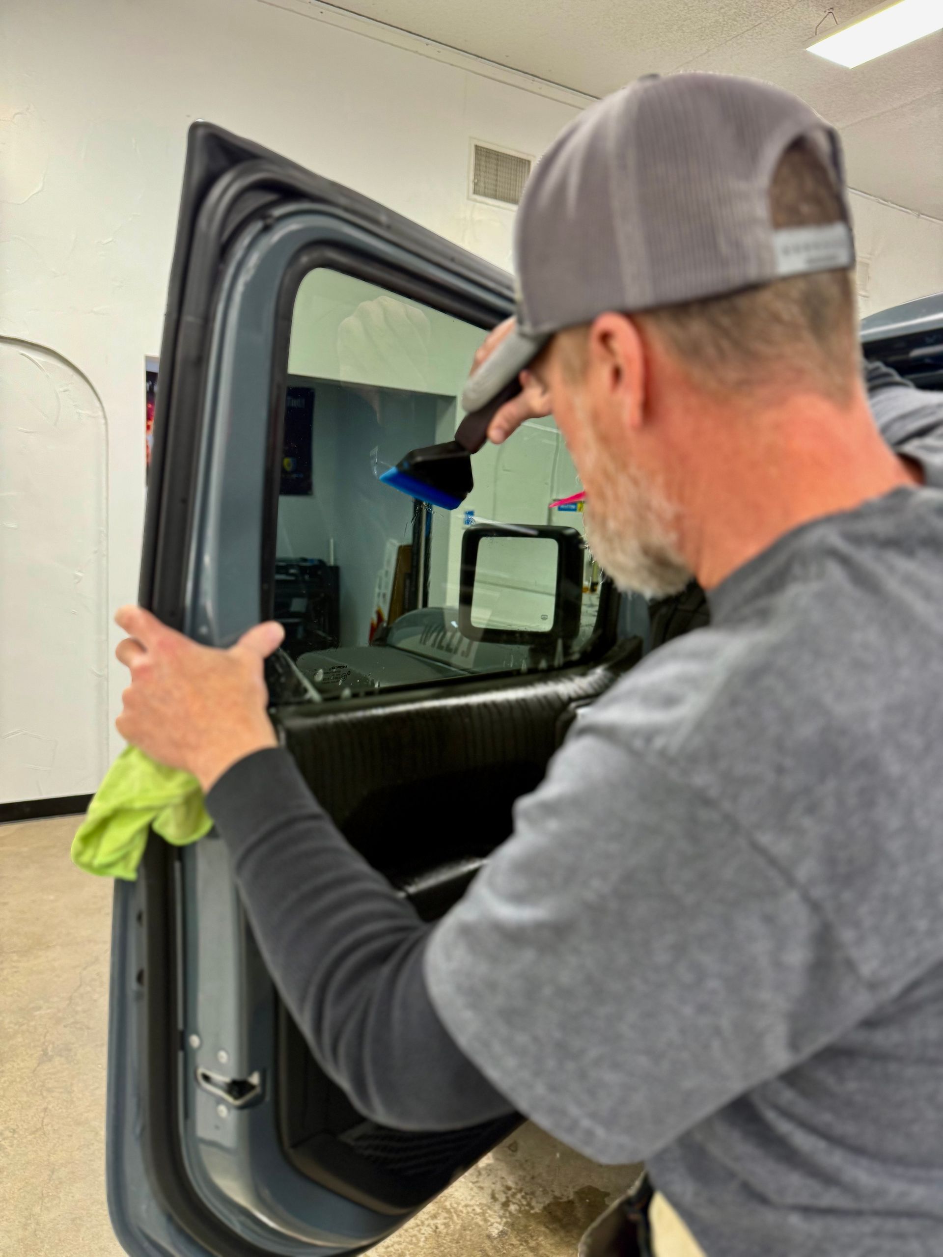 A person with tattoos on their arm wearing black gloves applies a clear protective film to the red fender of a truck.