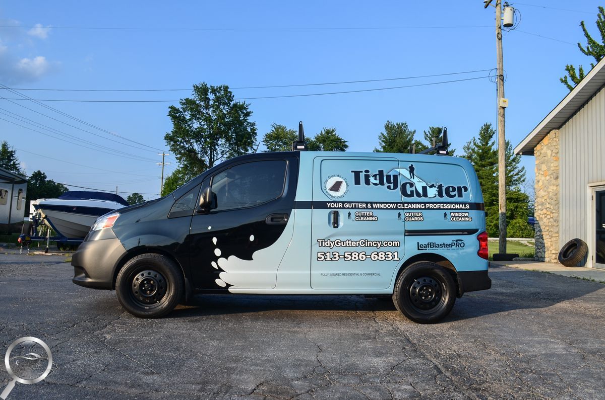 Damaged black-and-blue work van parked outdoors on gravel near a house and utility pole