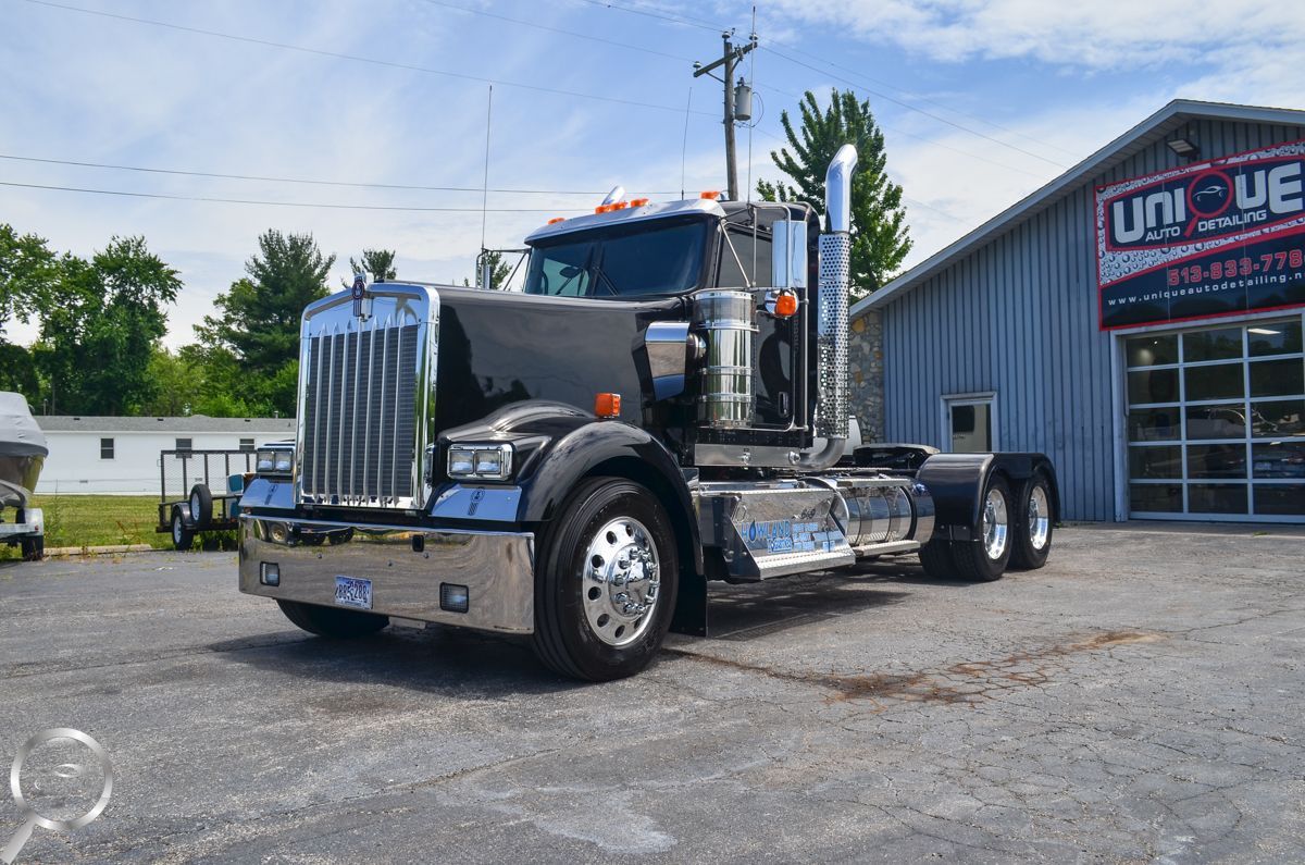Black semi-truck parked beside a gray building on a sunny day