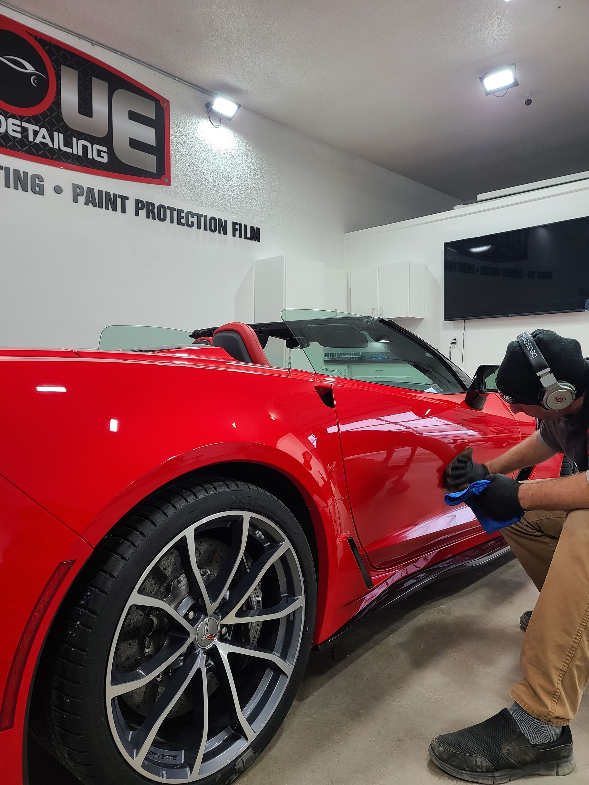 A person wearing gloves carefully polishes the side of a vibrant red sports car in a professional auto detailing shop.