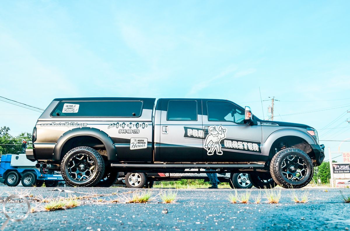 Black lifted pickup truck parked on grass under a bright blue sky with custom graphics and a camper shell