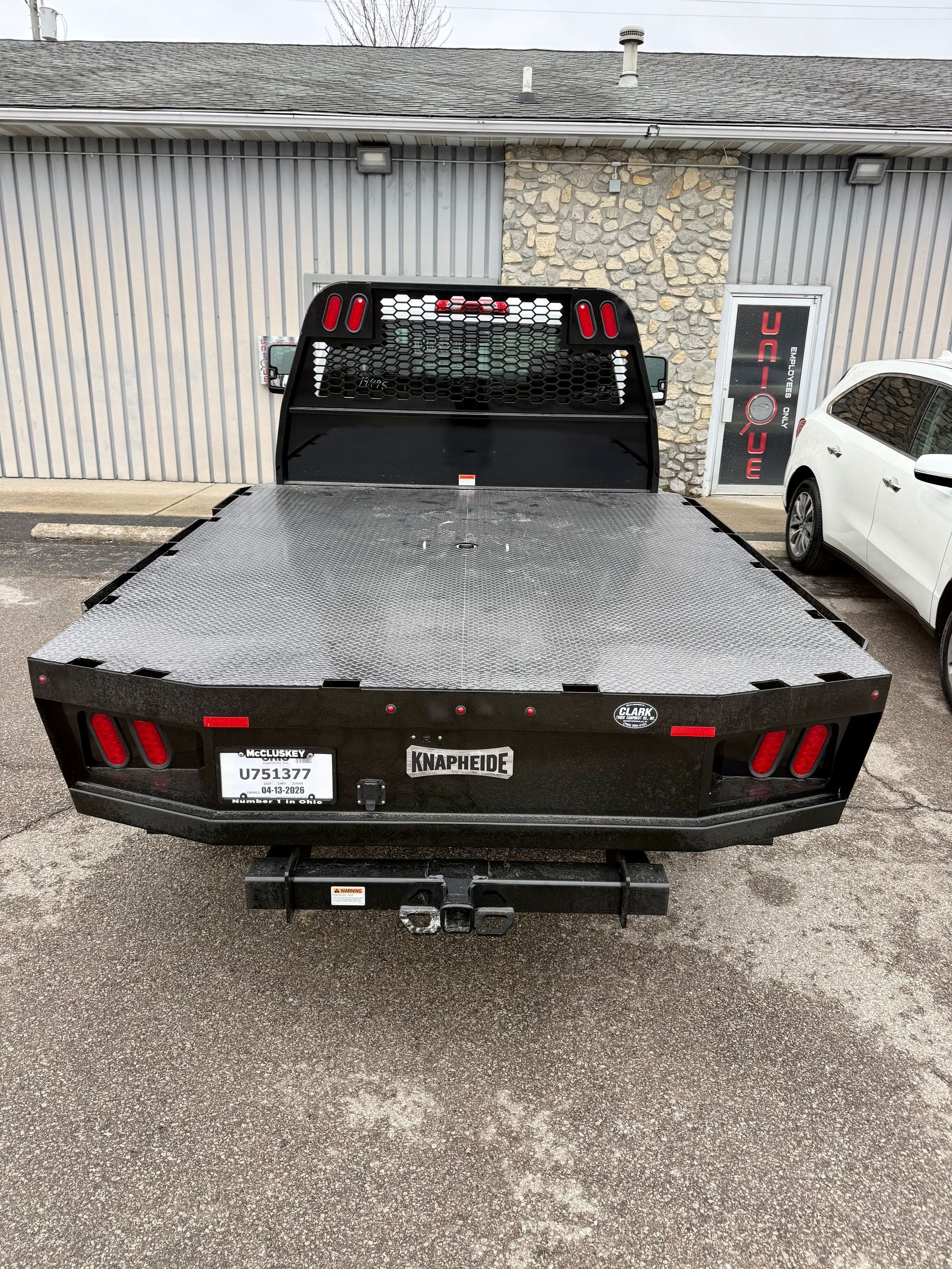 Black pickup truck parked in a driveway, rear view, with a textured bed cover and trailer hitch.