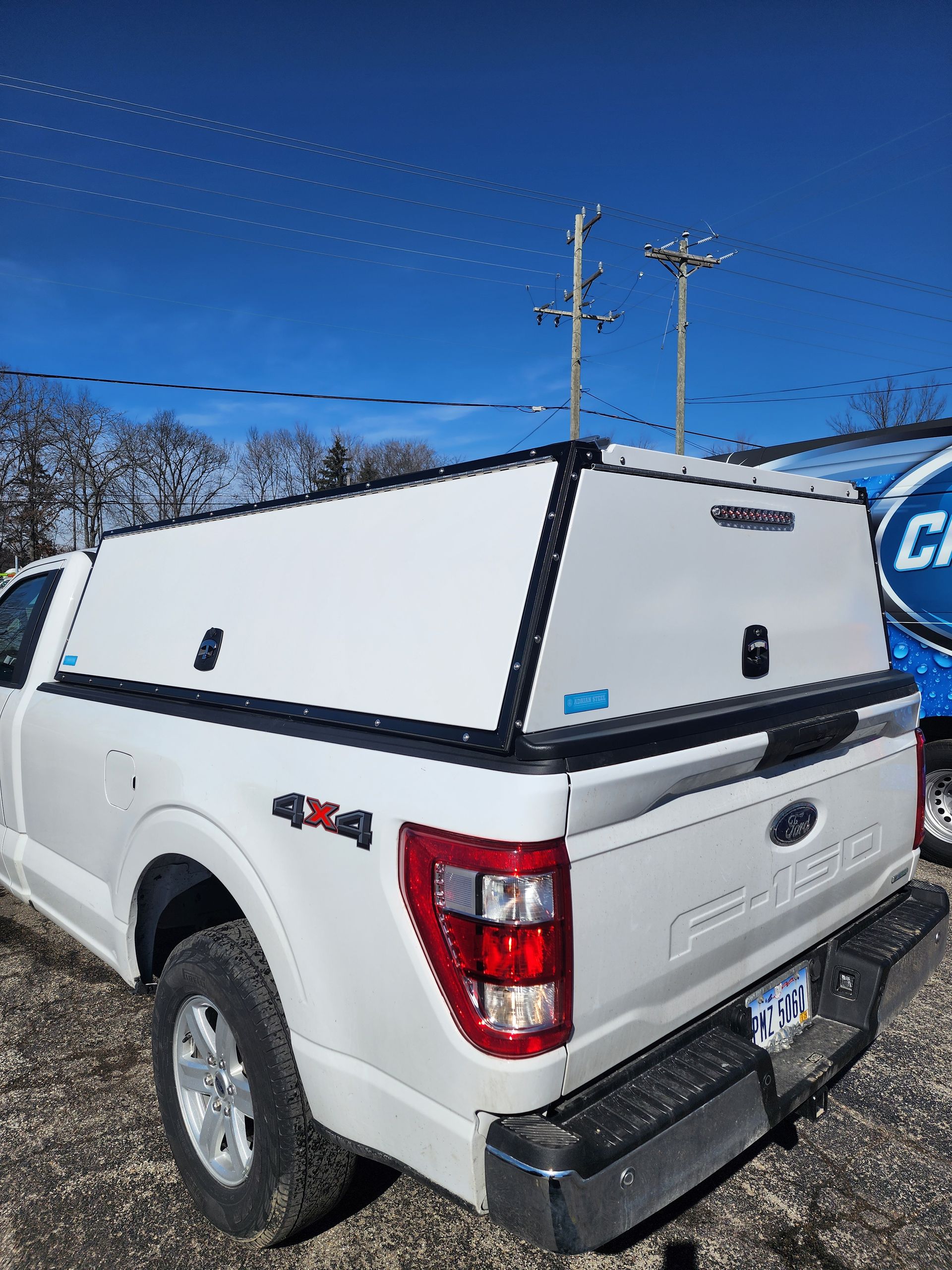 White pickup truck with a canopy and ladder rack parked outdoors under a blue sky.