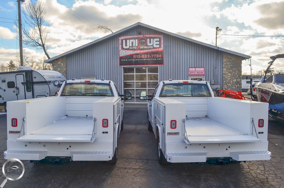 Two white service trucks parked in front of a Unive building on a snowy lot.