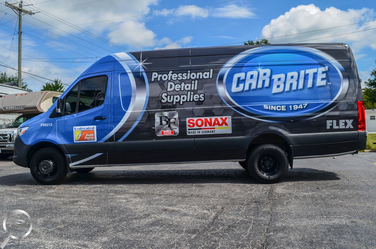 Blue and black CARBRITE service van parked on a roadside under a partly cloudy sky