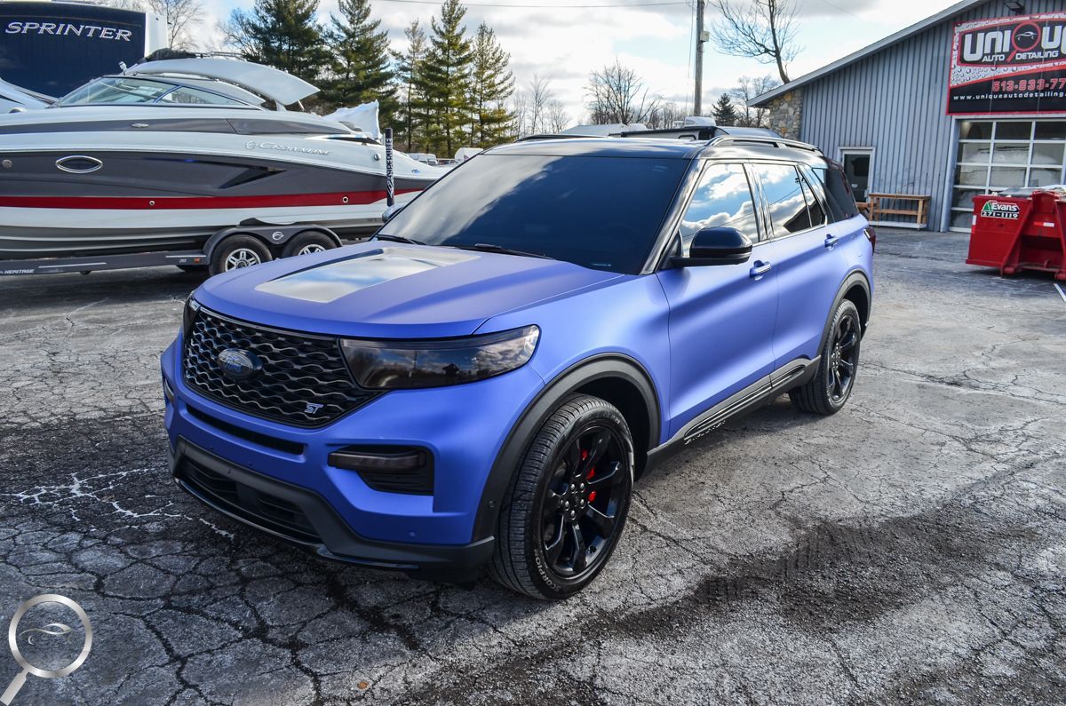 Blue SUV parked on a snowy lot outside a dealership, with tinted windows and black wheels