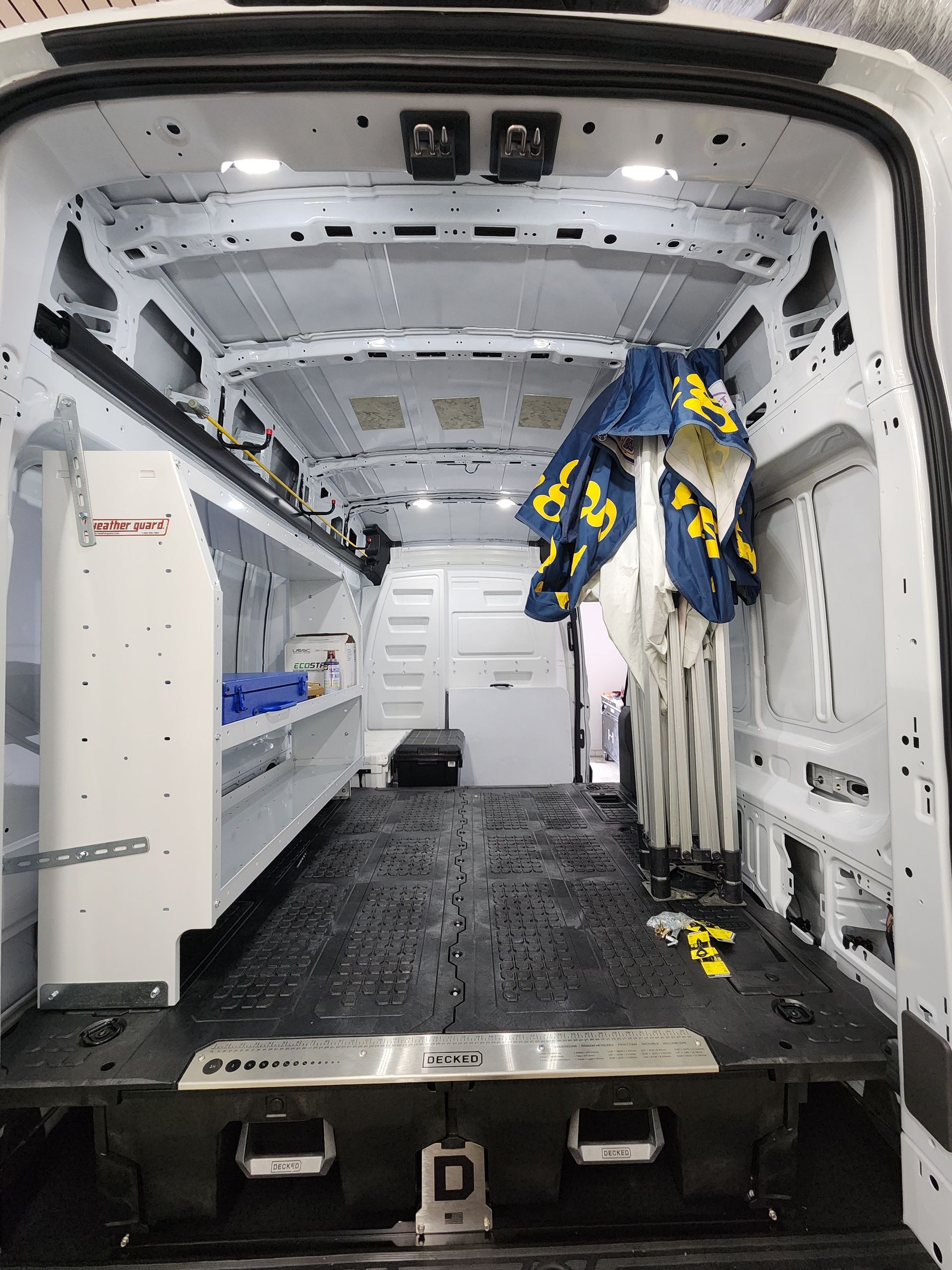 Interior of a white emergency van with equipment cabinets, bench seating, and hanging blue-yellow safety gear
