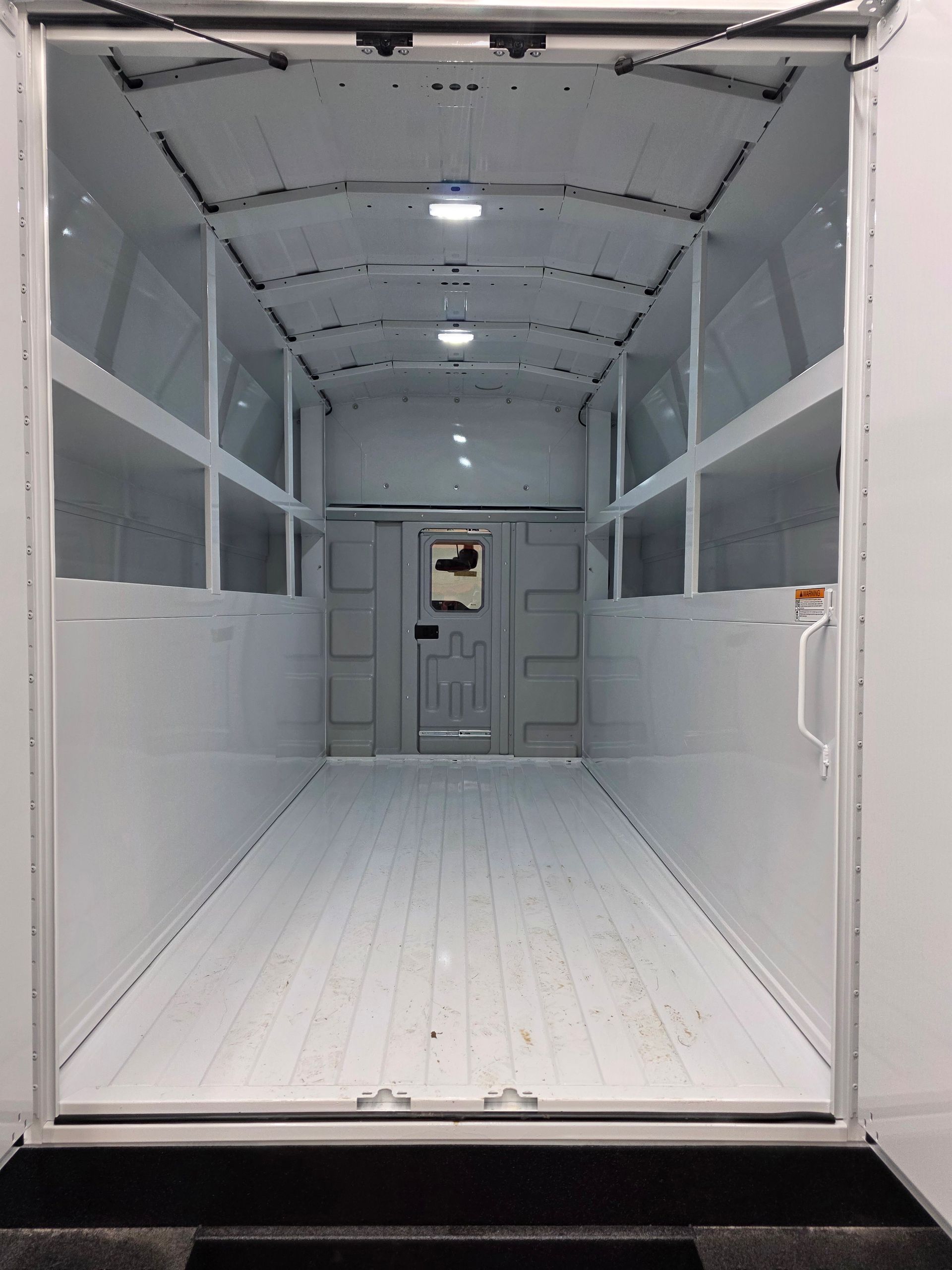Empty white cargo trailer interior with rear ramp door and side windows