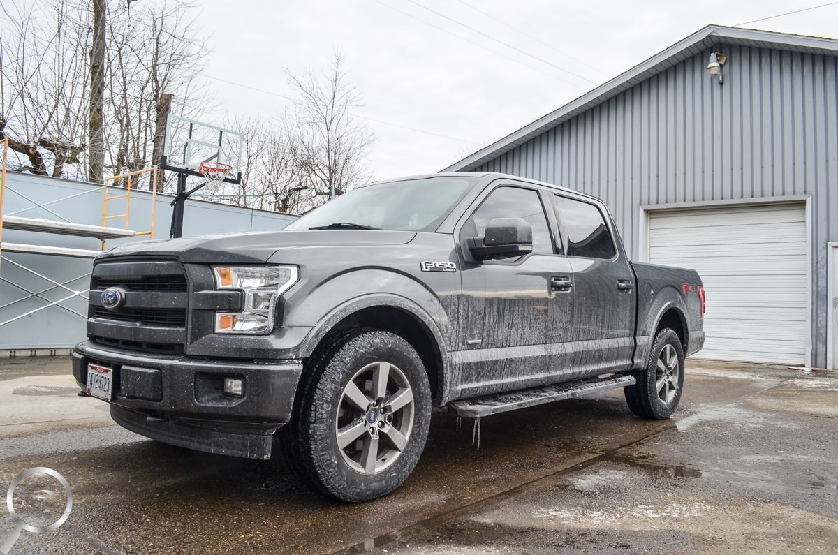 Black Ford pickup truck parked on a wet lot beside a gray garage on a snowy day