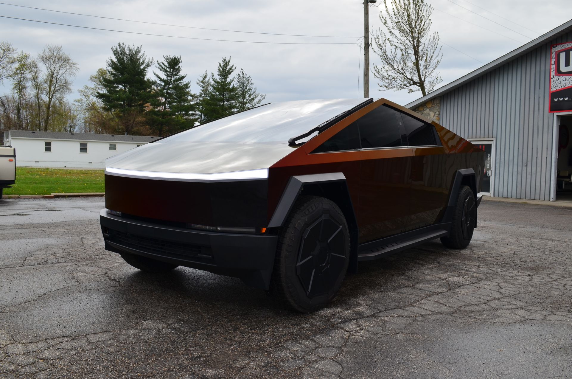 Cybertruck-style electric pickup with matte black and copper accents parked in a gravel lot under overcast skies
