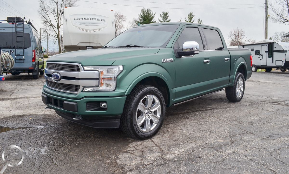 Green Ford pickup truck parked on wet pavement at a dealership