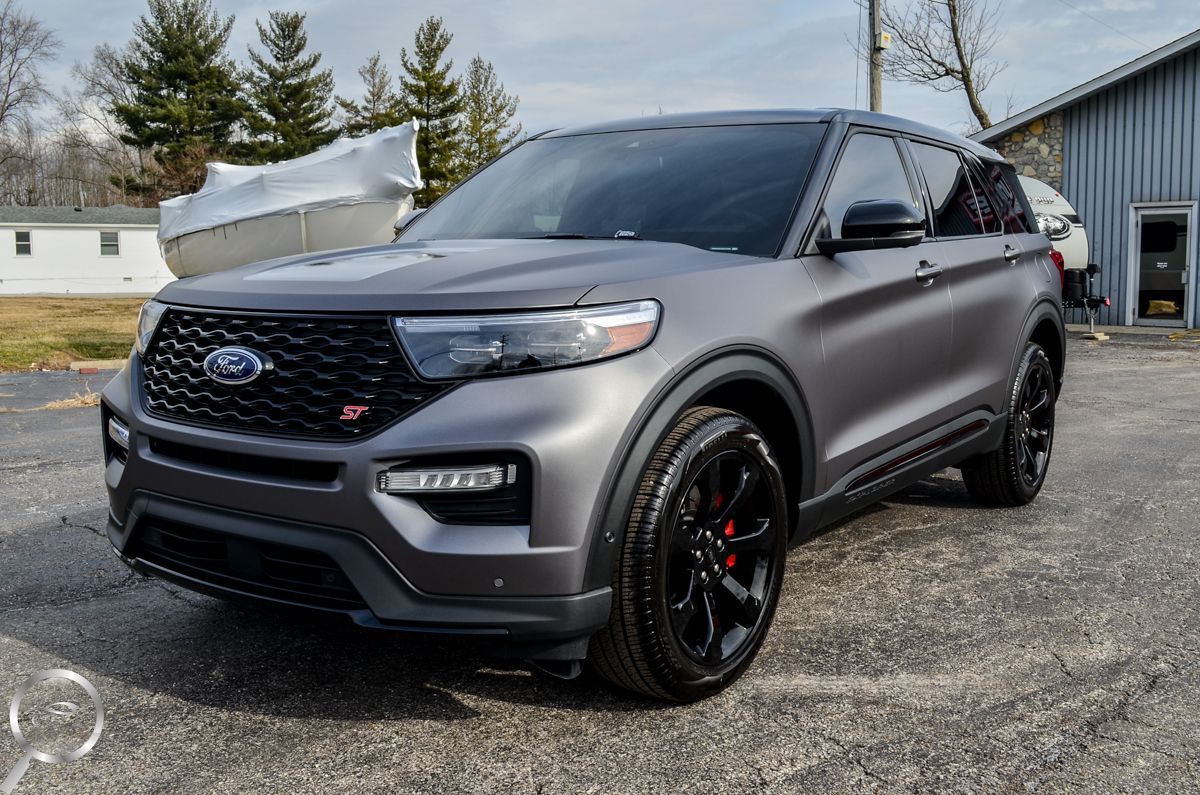 Matte gray SUV parked outdoors on gravel with black wheels and a wooded background