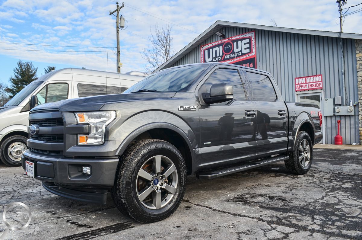 Dark gray pickup truck parked outside an auto shop on a wet lot