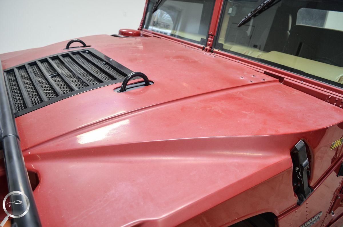 Red Jeep hood with black vents and windshield wipers, parked close to a building.