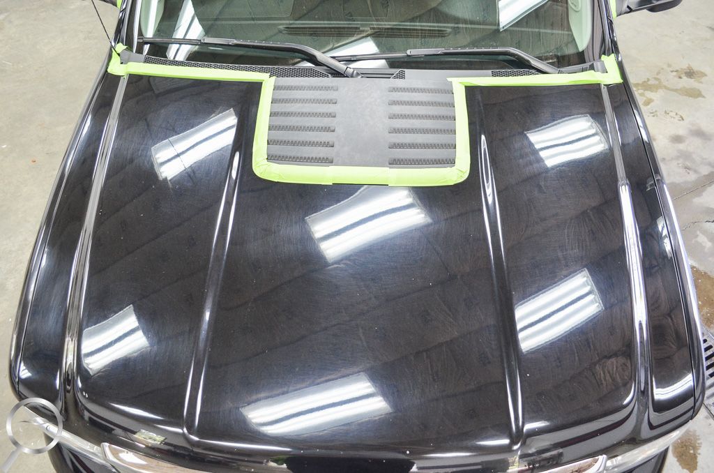Top view of a glossy black car hood with a green-trimmed vent near the windshield