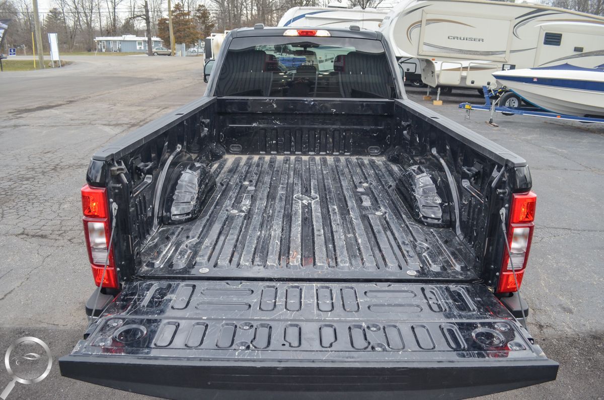 Open pickup truck bed with tailgate down in a parking lot, with trailers in the background.