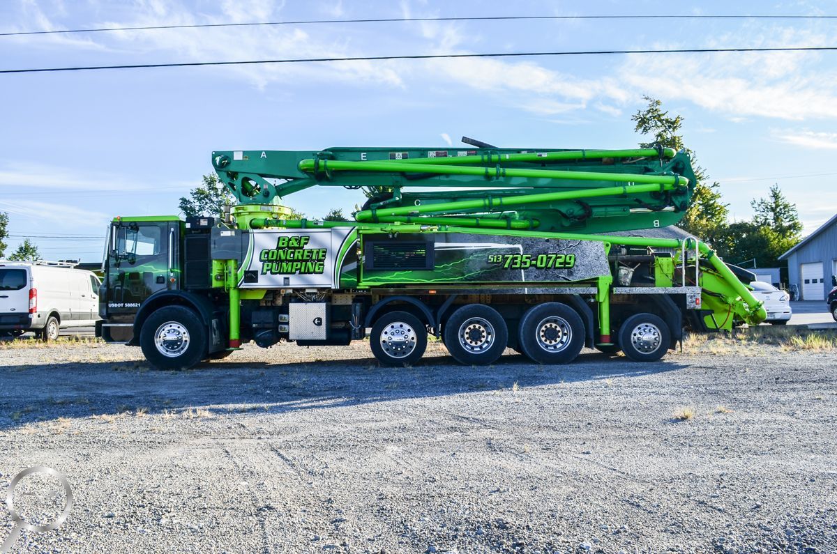 Green concrete pump truck parked on a gravel lot under a blue sky