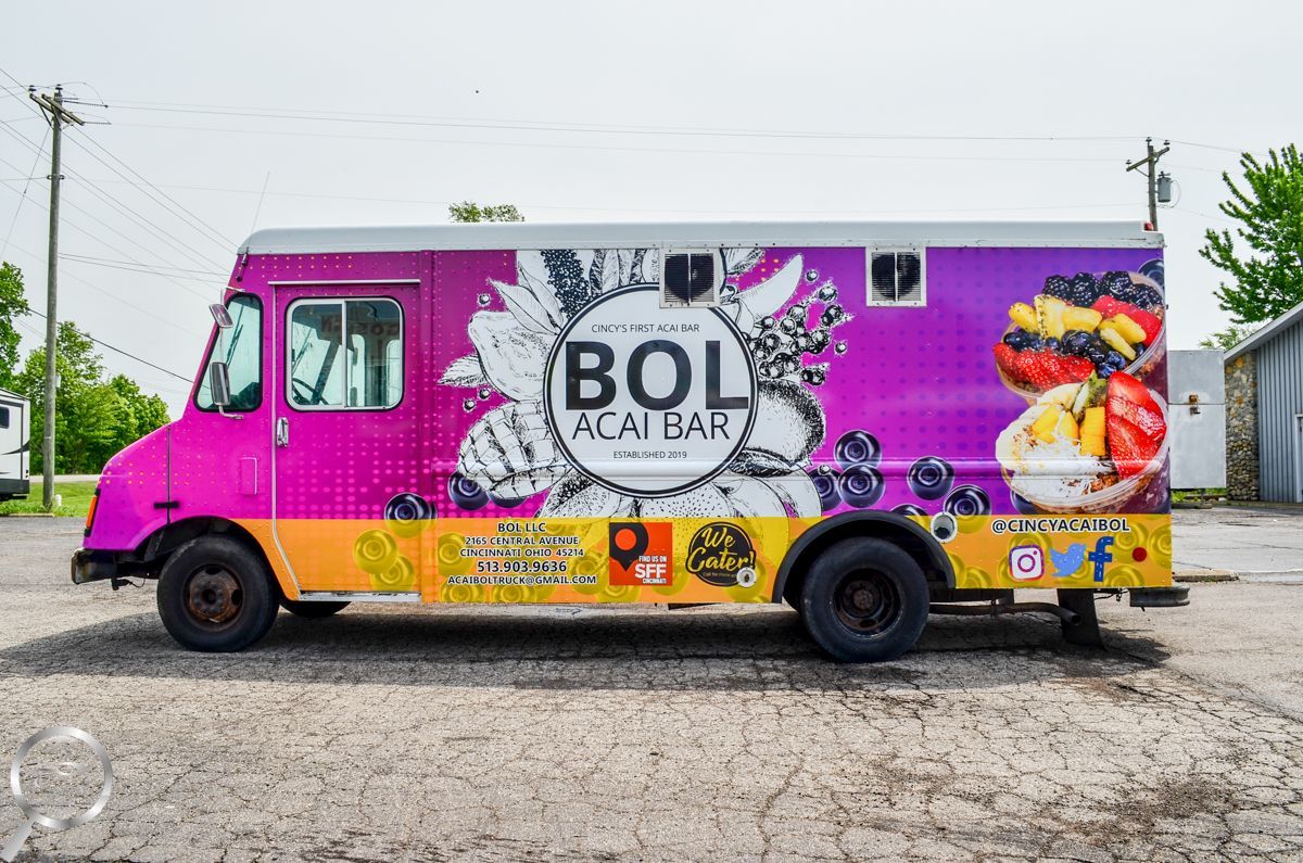 Bright pink and yellow Bol-themed food truck parked on gravel under cloudy sky