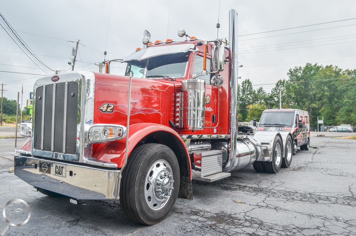 Red semi truck with chrome grille and trailer parked on a wet lot under overcast skies