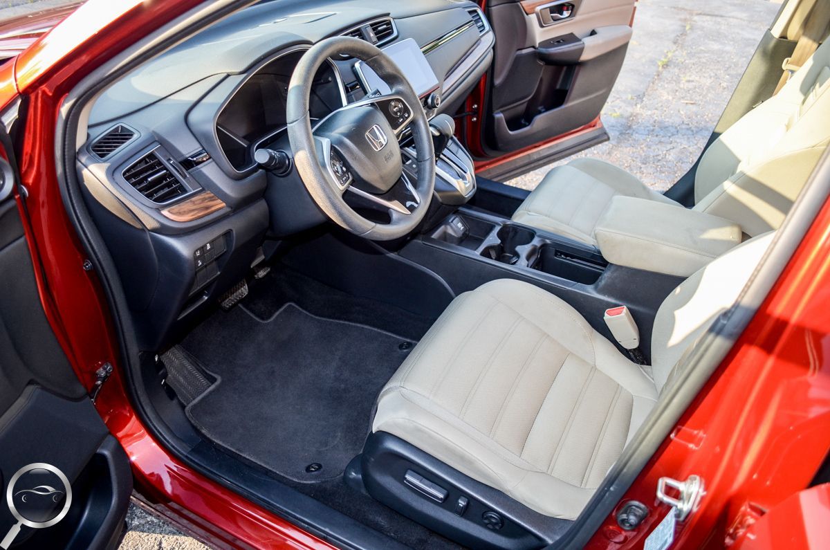 Red car interior with black dashboard, beige seats, and center console seen from open door
