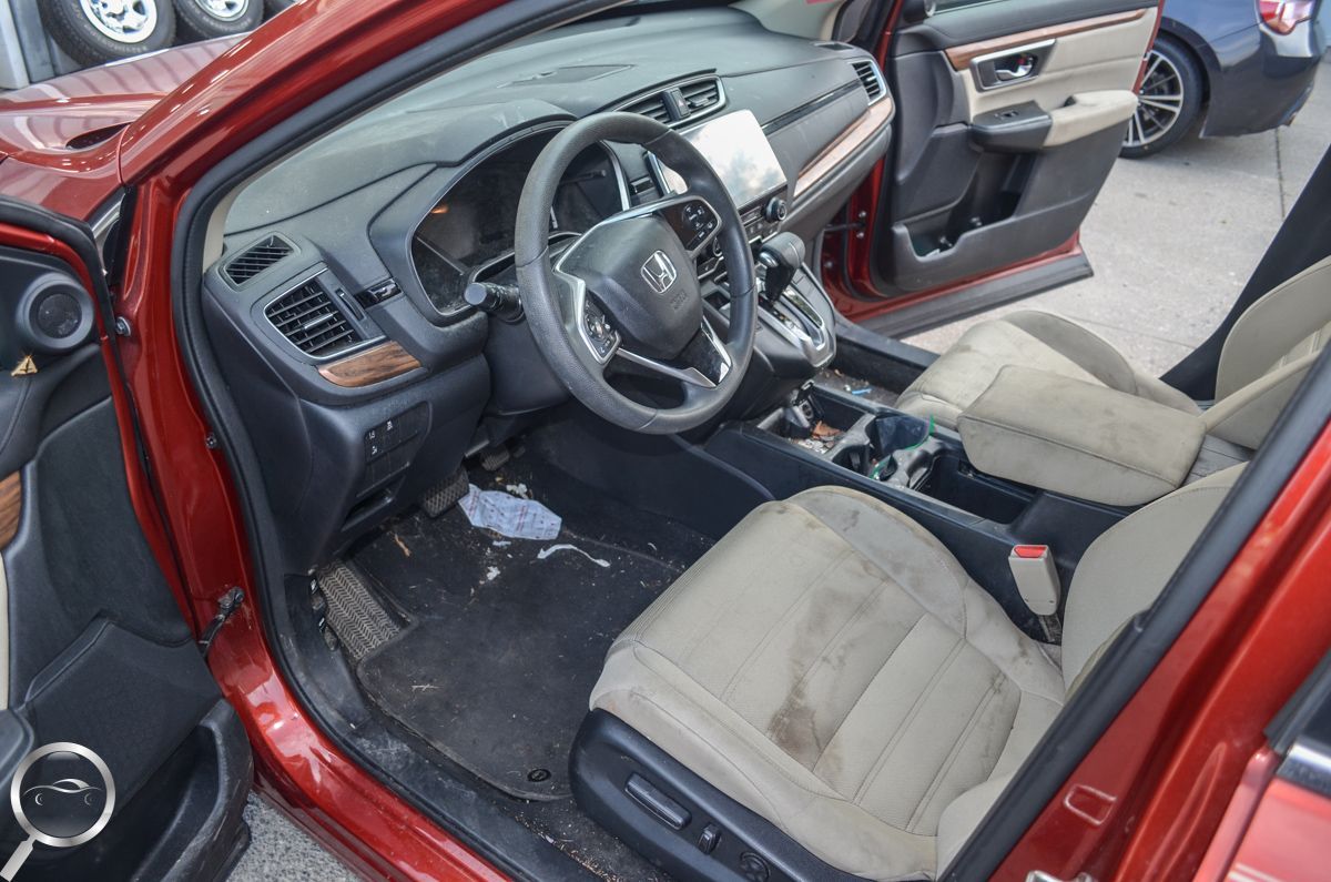 Open driver’s door of a red car, showing the black interior and front seats with some floor debris