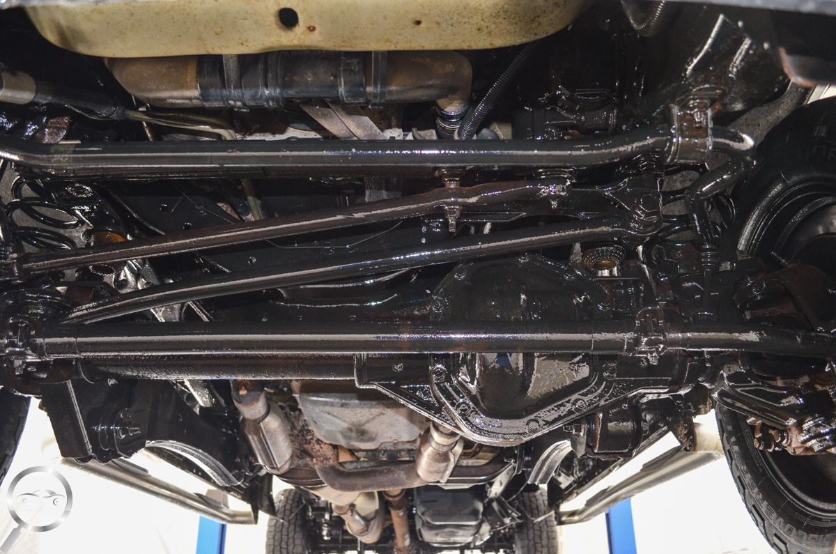 Undercarriage of a vehicle, showing the suspension, drivetrain, and exhaust components on a lift