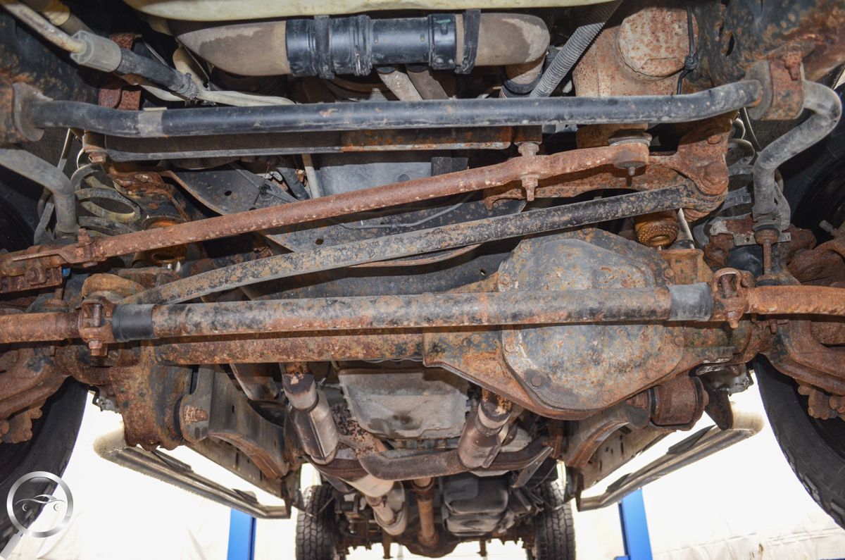 Undercarriage of a rusty vehicle, showing the axle, differential, and suspension parts.