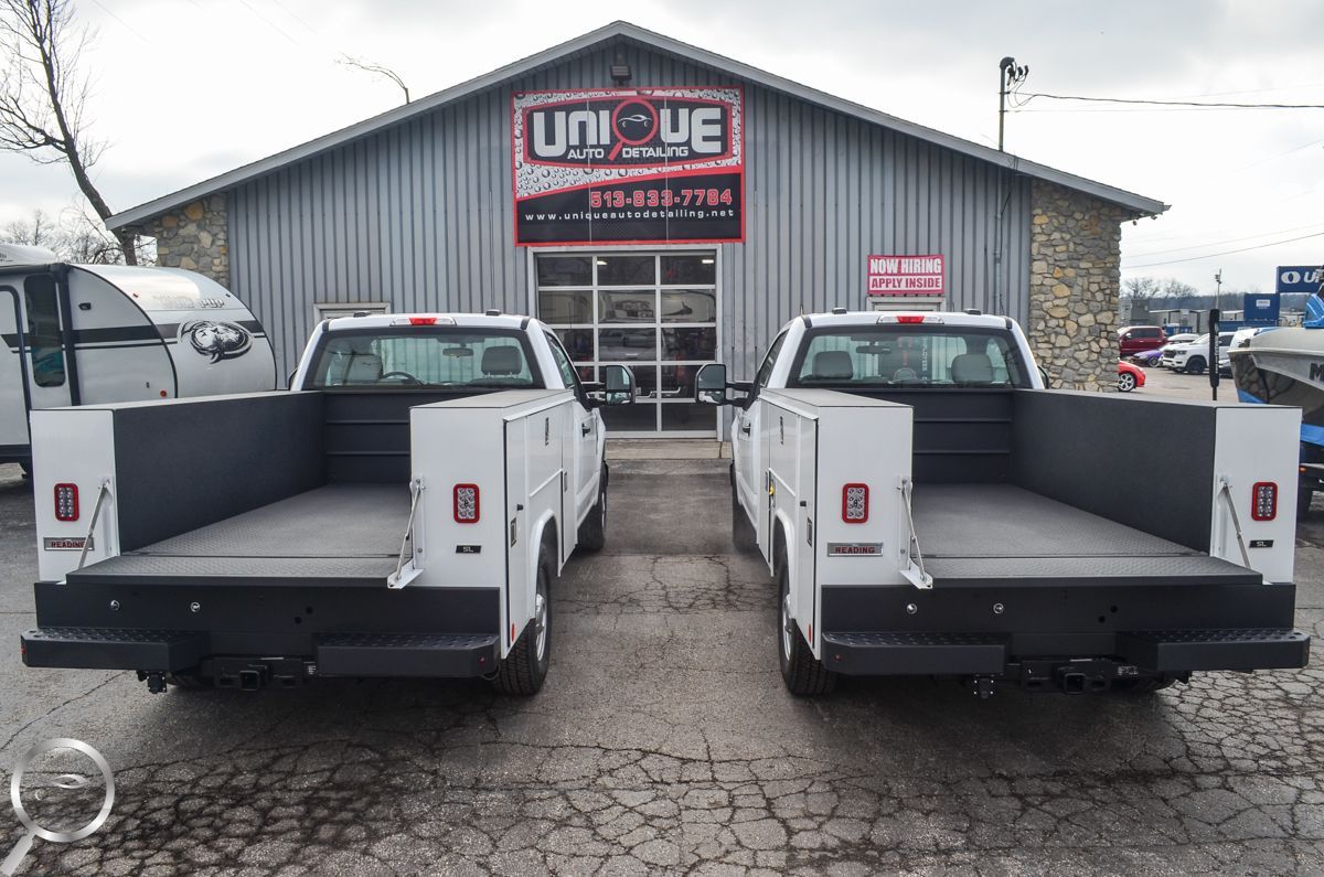 Two white pickup trucks parked in front of a gray auto shop with a UniQue sign.