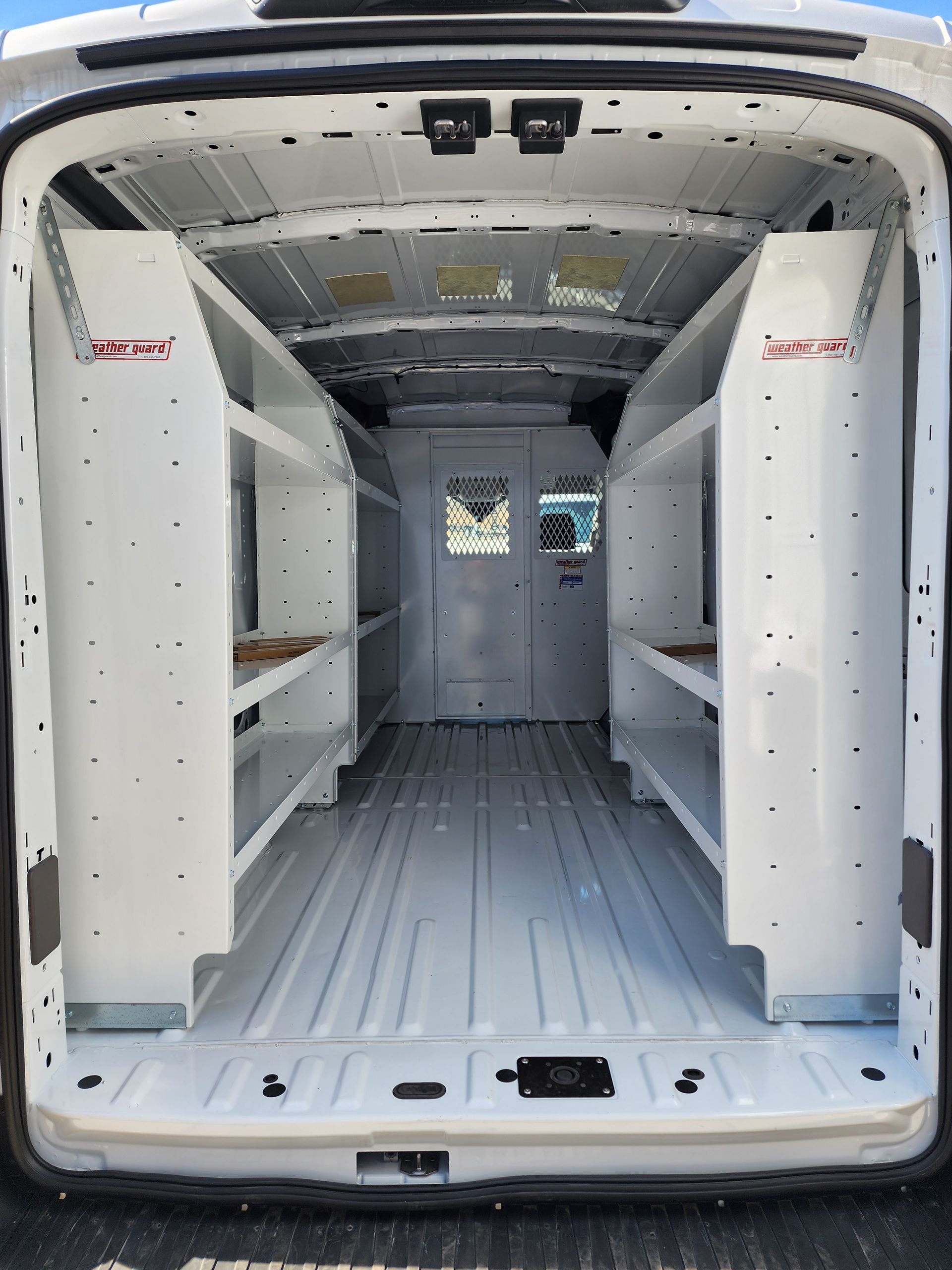 Empty cargo van interior with white shelving on both sides and rear doors open.