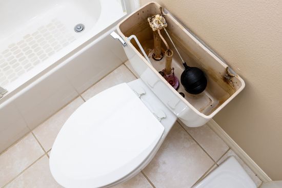 Toilet with tank open, revealing internal components. Bathroom setting with white fixtures and beige wall.