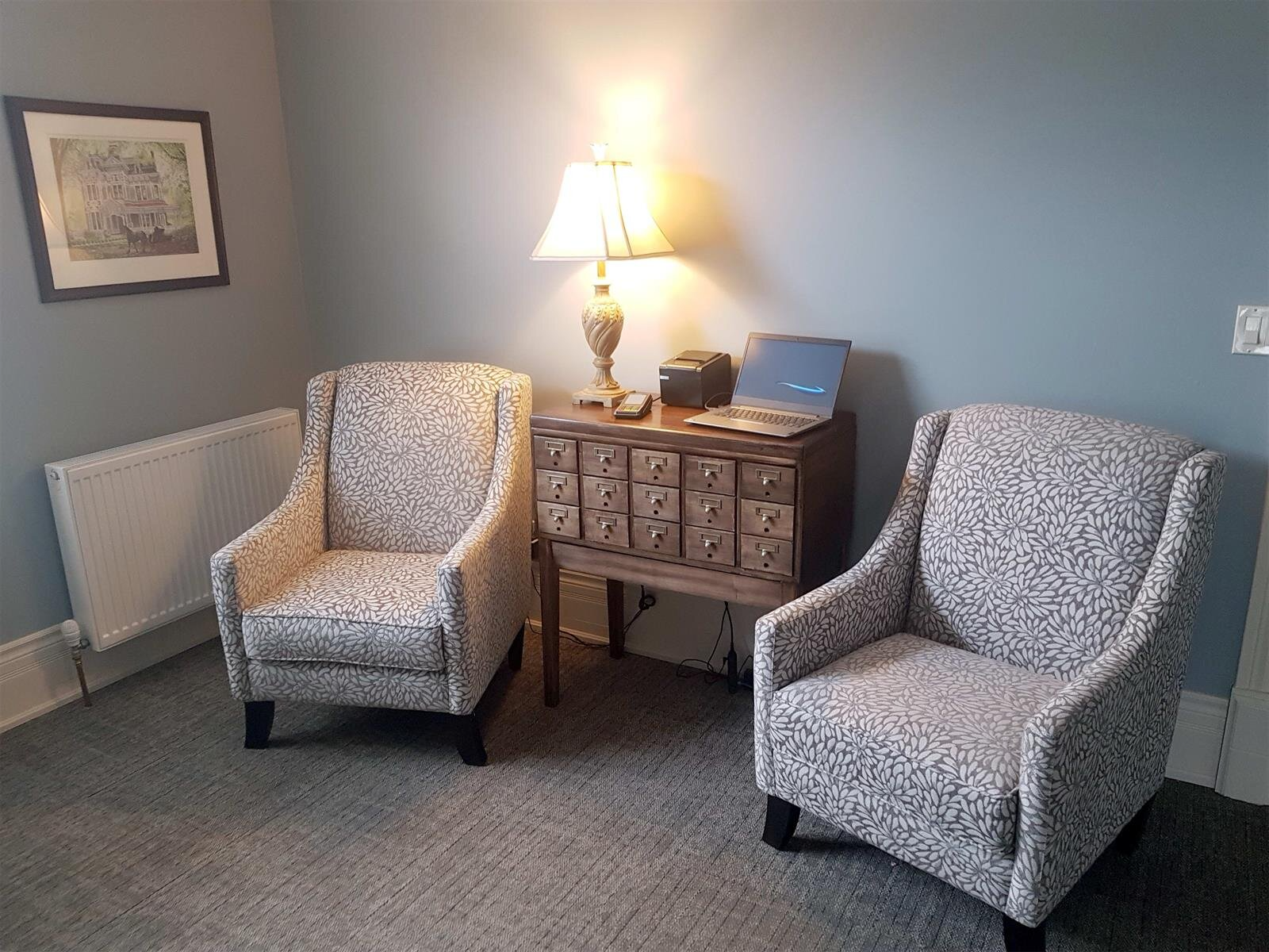 Two gray armchairs beside a lit lamp and wooden cabinet in a carpeted room