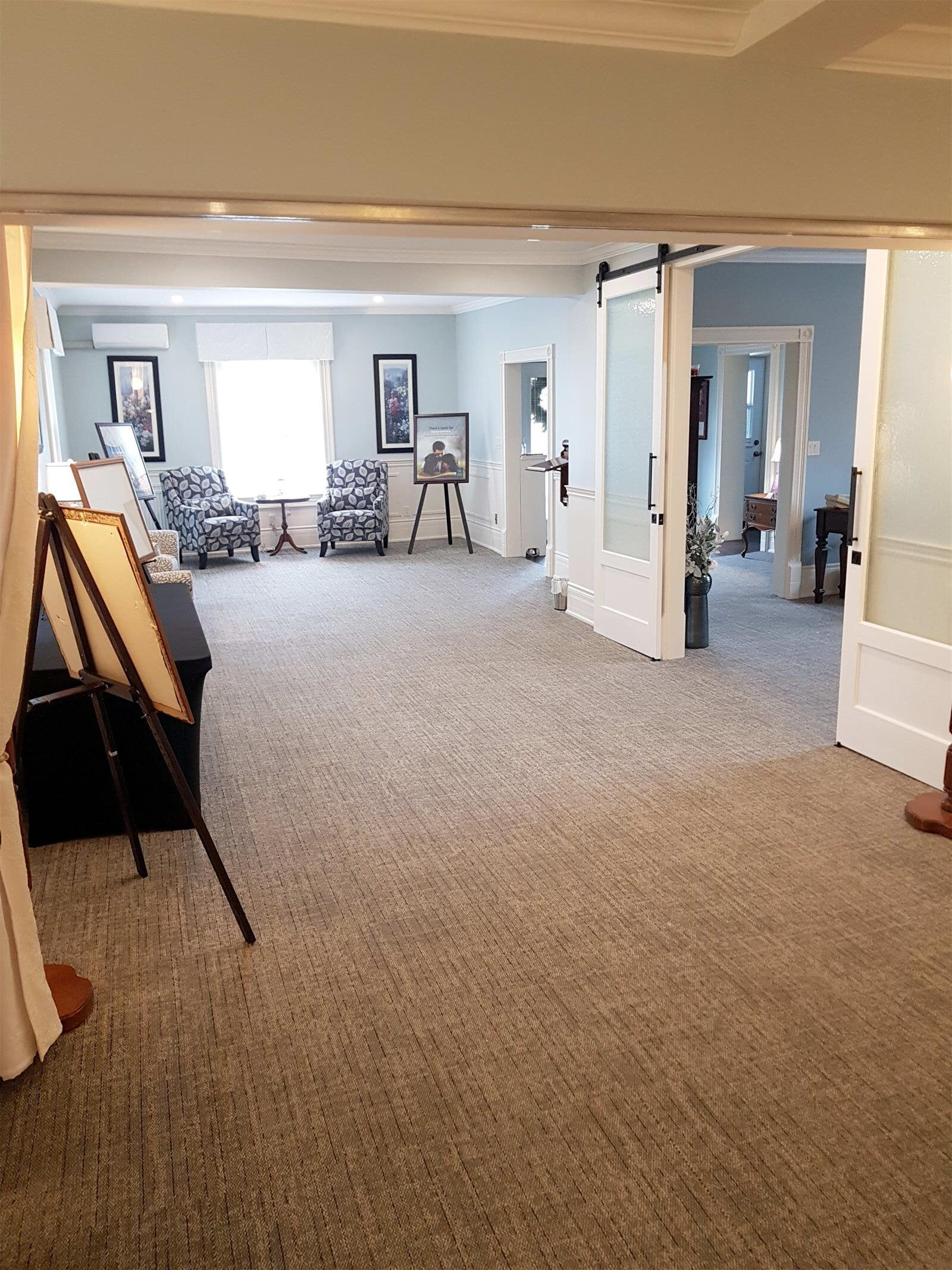 Spacious beige-carpeted room with white walls, chairs near windows, and open doorways to adjoining rooms
