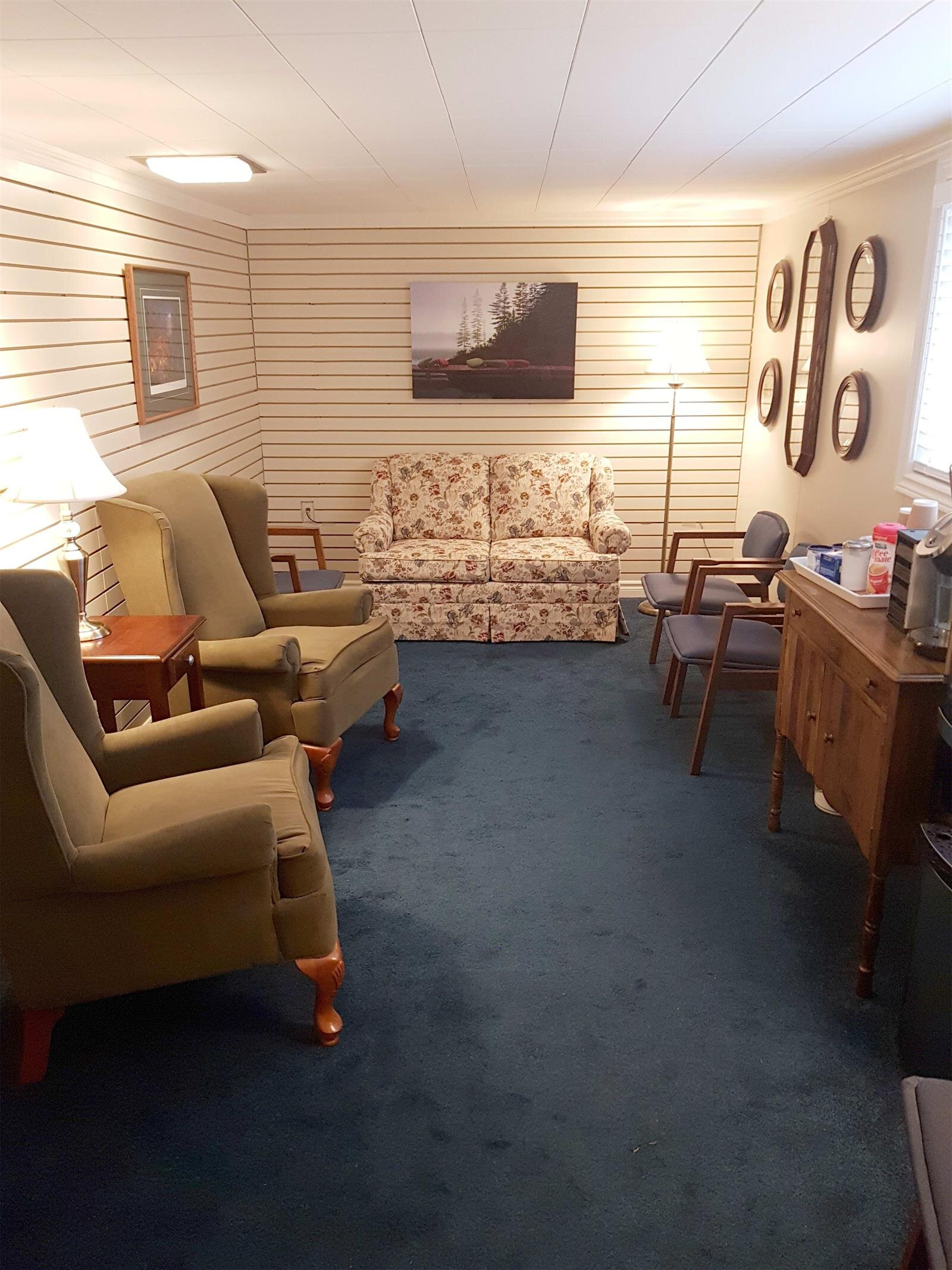 Cozy living room with blue carpet, patterned sofa, armchairs, and wooden side table under warm lighting