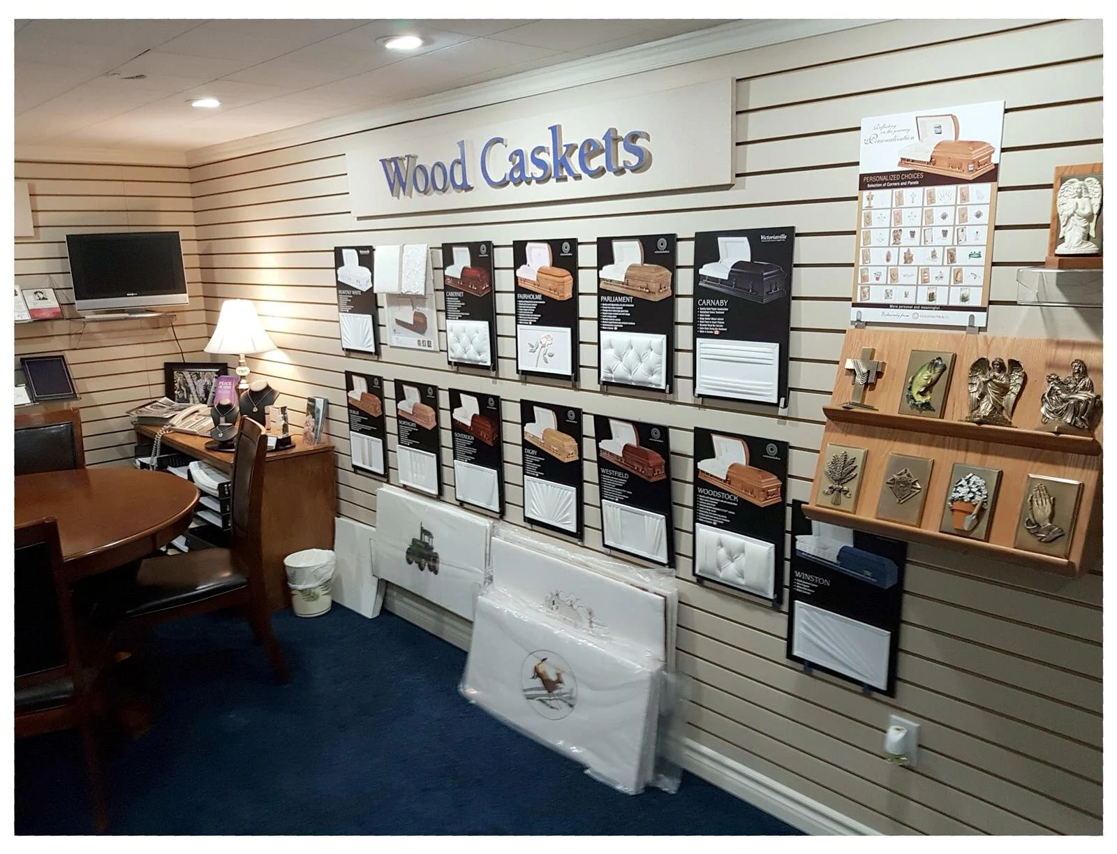 Display of wood caskets and funeral brochures in a showroom with slatwall shelves and a blue carpet.