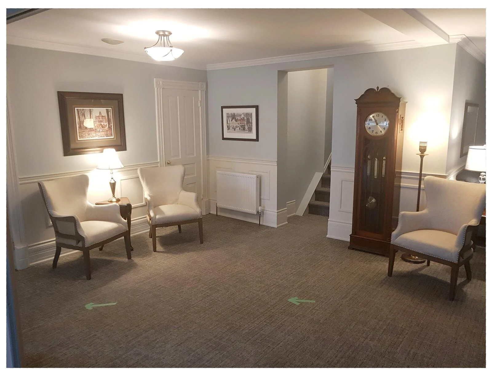 Elegant living room with chairs, lamps, grandfather clock, and framed artwork on beige walls