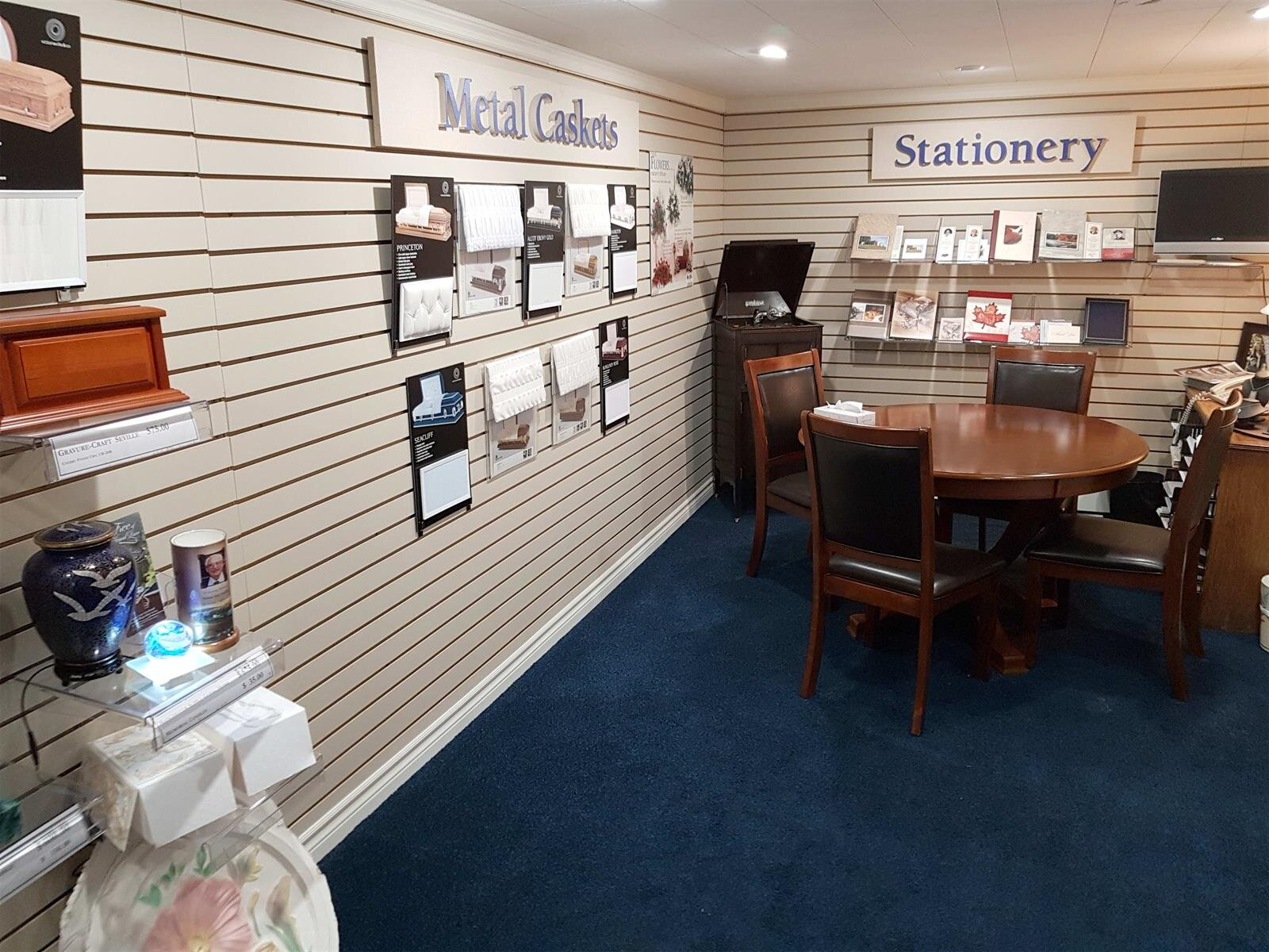 Small gift shop interior with blue carpet, slat walls, wooden table, and signs for metal cards and stationery.