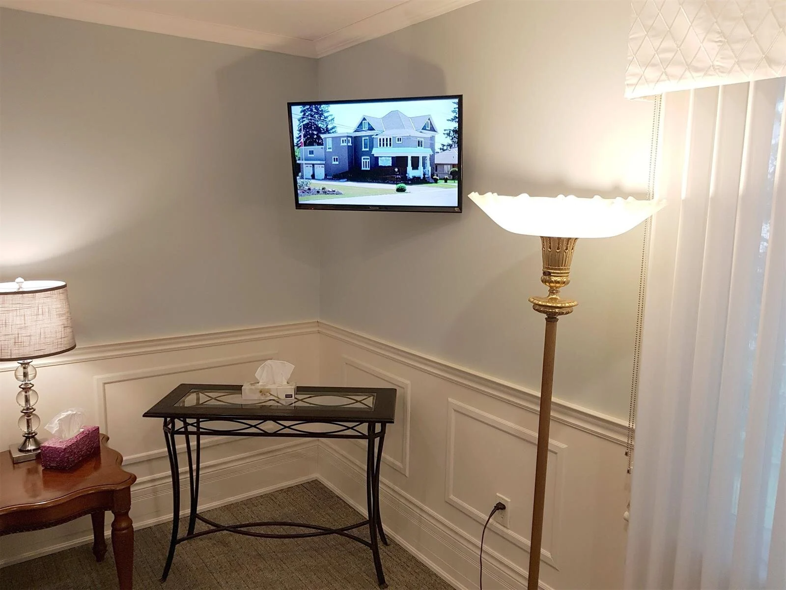 Living room with wall-mounted TV, floor lamp, small table, and vertical blinds in a corner space