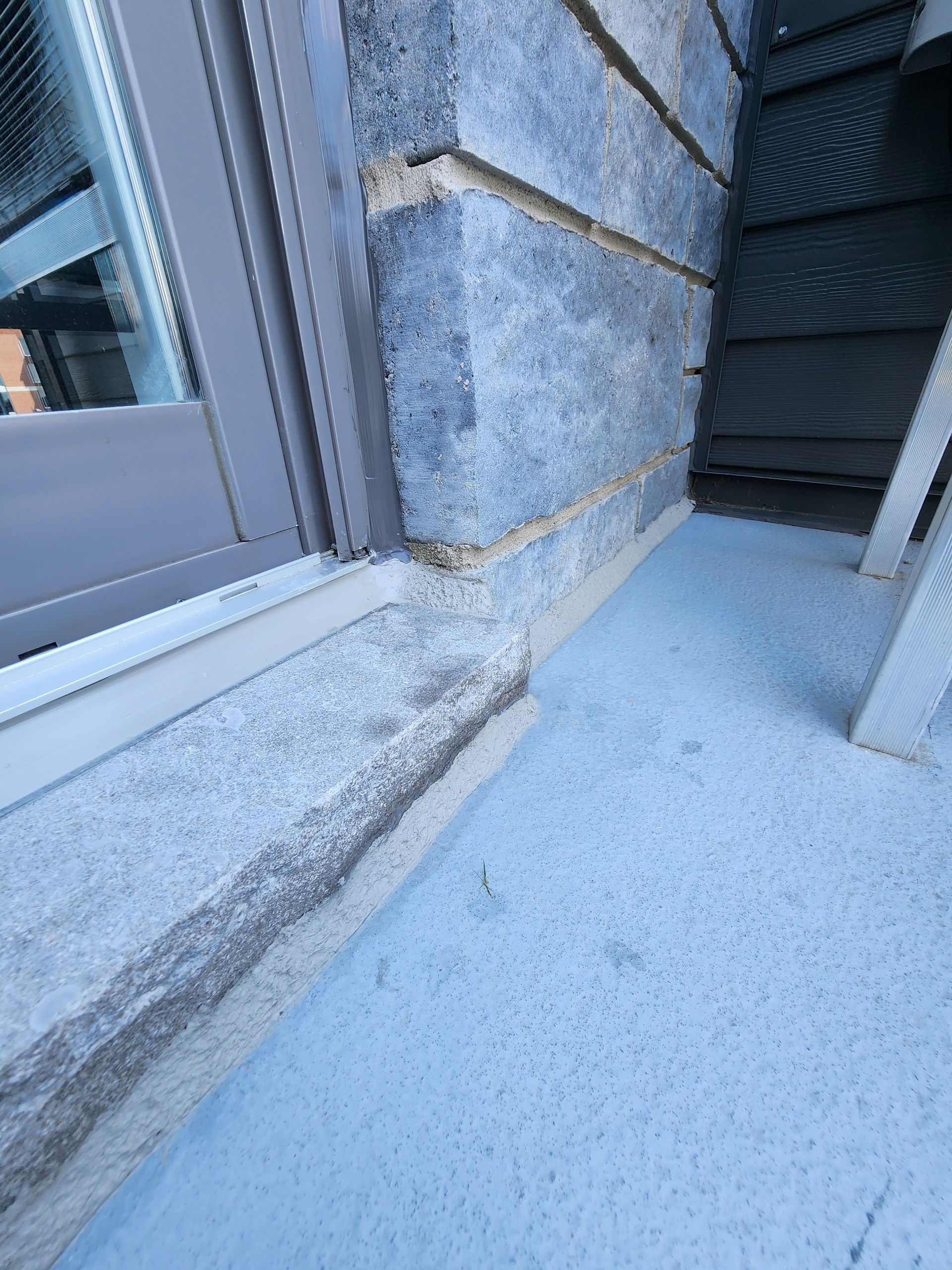 Vue extérieure d'une fenêtre avec encadrement en béton et mur en briques.