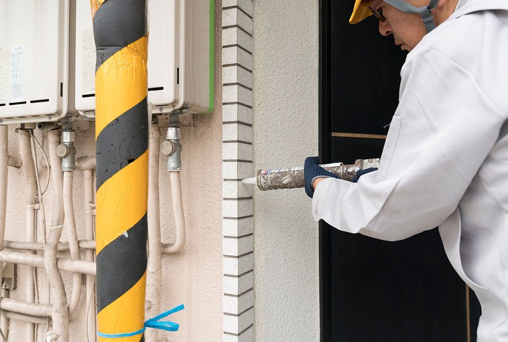 Un ouvrier du bâtiment en uniforme blanc scelle un coin de bâtiment avec un pistolet à calfeutrer.