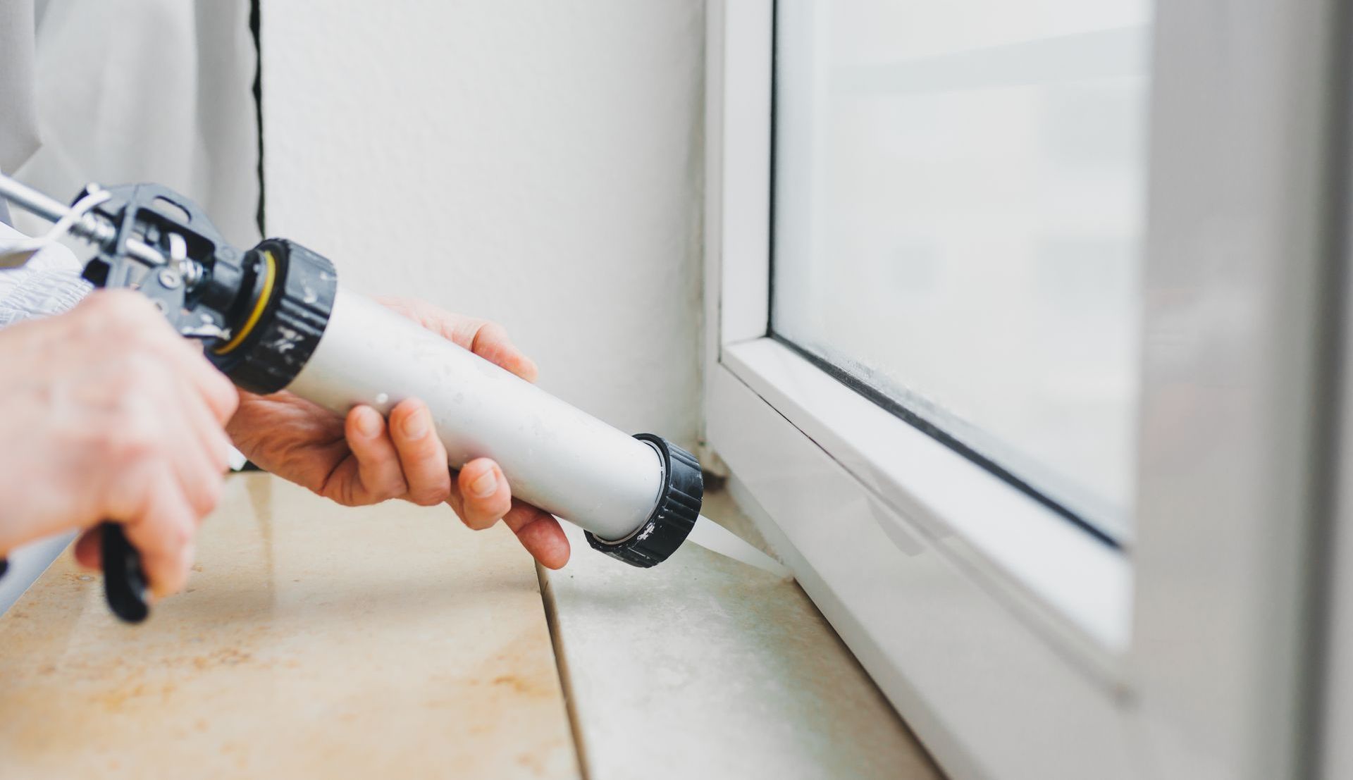 Personne appliquant du mastic sur un cadre de fenêtre blanc à l'aide d'un pistolet à mastic.