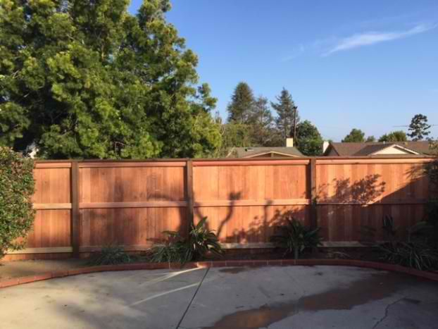 A wooden fence surrounds a concrete patio with trees in the background.