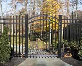 A wrought iron gate is surrounded by a fence and trees.