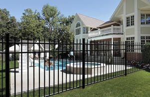 A man is swimming in a pool behind a fence in front of a large house.
