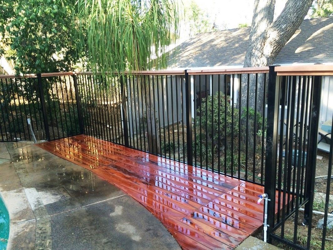 A wooden deck with a metal railing and a pool in the background.
