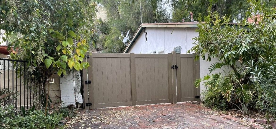 A wooden gate is surrounded by trees and bushes in front of a house.