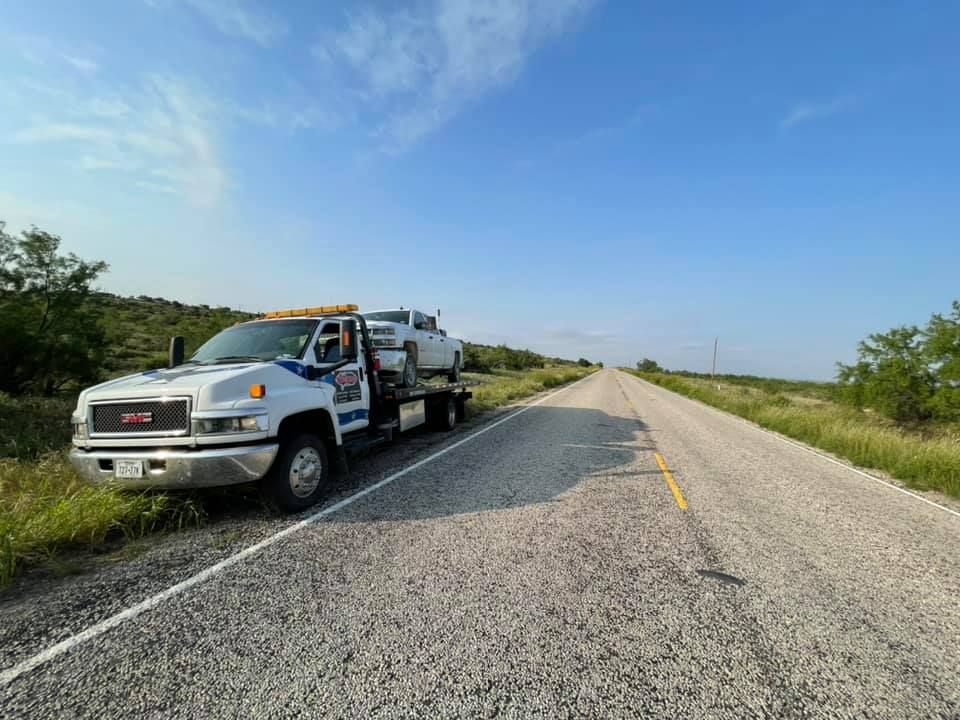 Tow truck with a car on its flatbed parked on a rural road under a blue sky.