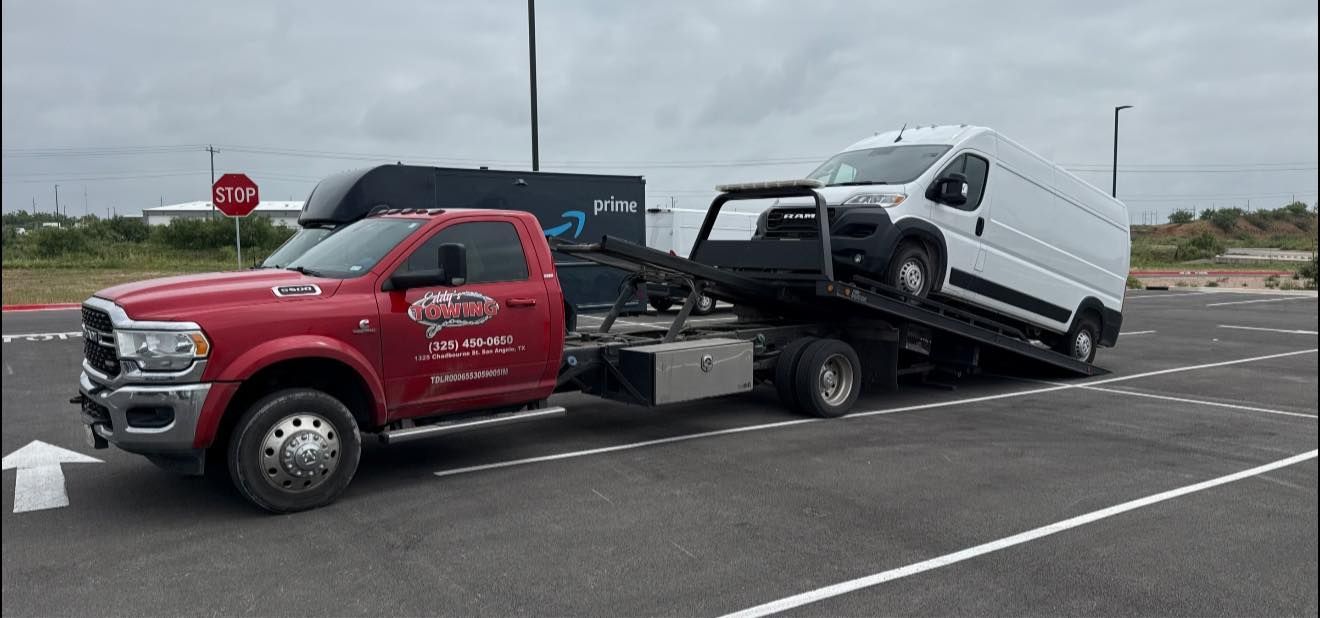 Red tow truck transporting a white van on a gray asphalt lot.