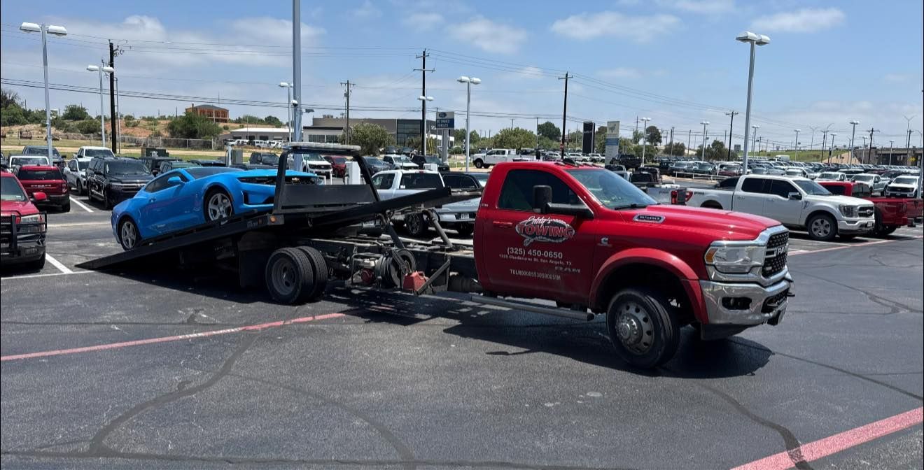Red tow truck with a blue car on its flatbed in a parking lot.